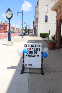 A street sign reading "Celebrating 130 years join us Friday!"