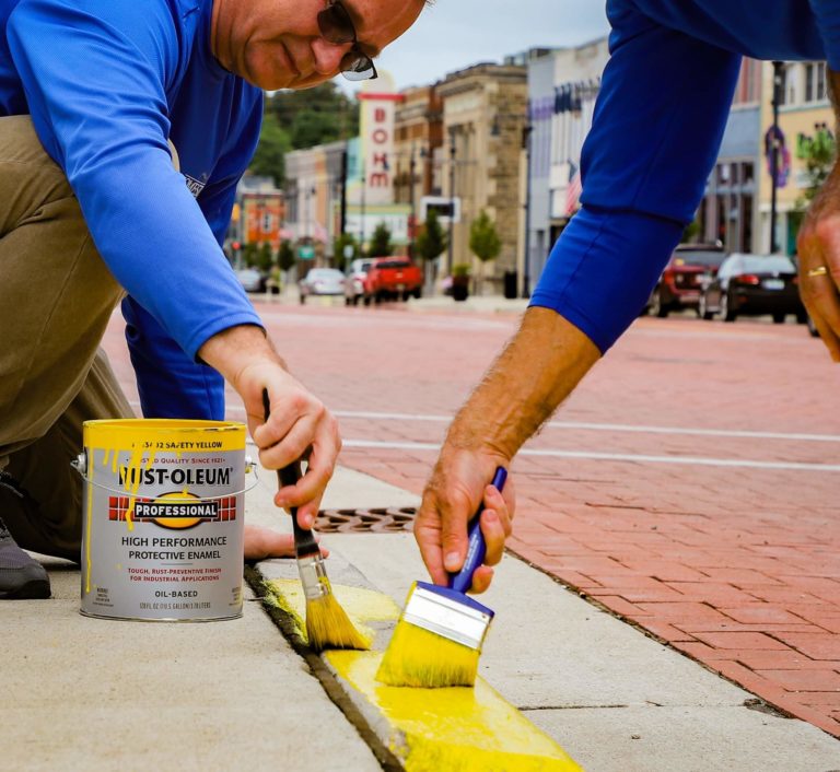 The hands of two Homestead Savings Bank employees as they repaint the border of the sidewalk yellow for Community Unity Day.