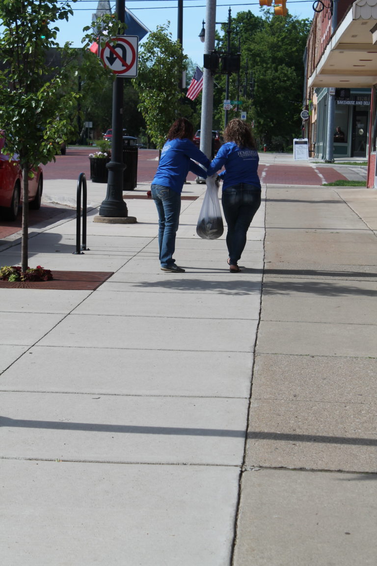 Two members of the the Homestead team carrying mulch down the street.
