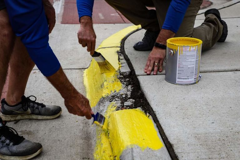 The hands of two Homestead Savings Bank employees as they repains the border of the sidewalk yellow for Community Unity Day.